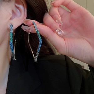 Macro shot of silver needle geometric hoop earrings with blue-green gradient rhinestones