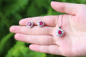 Detailed view of silver necklace and earrings set with round red rubies on palm