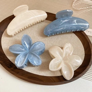 Détail de pinces à cheveux à fleurs en acrylique bleu et crème sur un plateau en bois