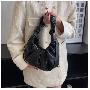 Close-up of black pleated leather underarm bag with glossy finish on a cream jacket