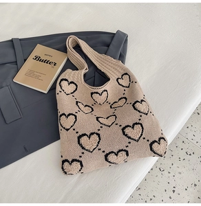 Détail du sac à main tricoté beige à motifs de cœurs posé sur une surface en tissu doux