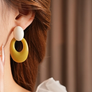 Close-up of a model wearing retro oval hollow earrings in white and yellow acrylic