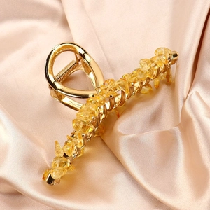 Detail of a golden metal hair claw clip featuring inlaid raw yellow crystal stones