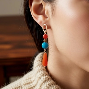 Detail of vintage beaded earrings with orange teardrop pendant on a model wearing knitwear