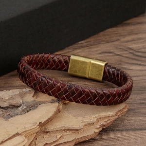 Detail of brown braided leather bracelet with gold magnetic clasp on a rustic wood surface