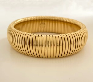Detail of golden Tubogas wide bracelet with ribbed texture on reflective surface