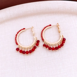 Detailed close-up of ethnic style gold hoop earrings with red beads and woven thread