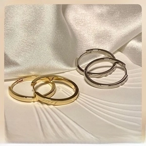 Detailed close-up of gold and silver polished hoop earrings on elegant beige silk fabric