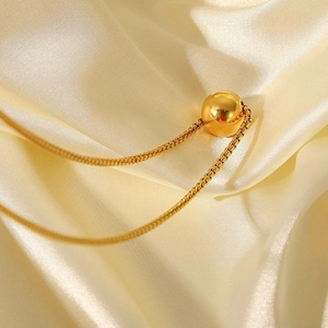 Macro shot of minimalist gold ball pendant with sleek snake chain on ivory silk fabric