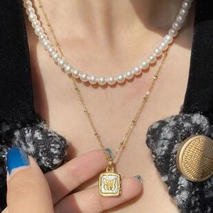 Detail of layered gold chain and pearl necklace with a square butterfly charm pendant