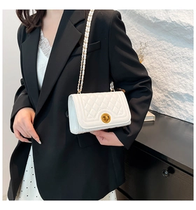 Detail of white quilted crossbody bag with gold round lock and metal chain strap