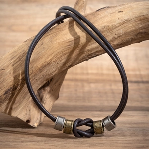 Detail view of a leather beaded necklace with metal charms on a rustic wooden branch