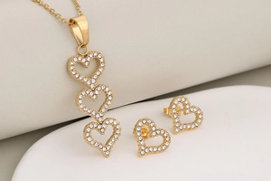 Macro detail of gold-tone triple hollow heart pendant and matching rhinestone stud earrings