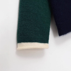 Gros plan sur le pull en tricot bicolore vert et bleu avec poignets en bord-côte blanc