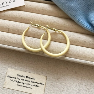 Detail of matte pale yellow hoop earrings on a beige striped velvet jewelry tray