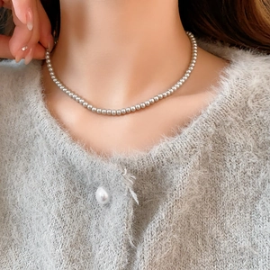 Detail of 4mm gray pearl necklace showing metallic luster on a knitted fabric background
