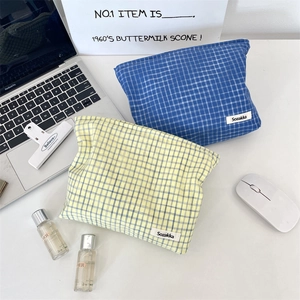 Blue and green checkered cosmetic bags shown on a desk with a laptop and skincare items