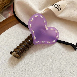 Détail d'une pince à cheveux cœur en acrylique violet avec coutures jaunes sur fond textile