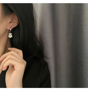Detail of silver drop earrings with hollow bear and iridescent flower charm on a model