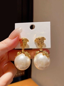 Dettaglio di orecchini vintage in oro con medaglione a rilievo e grandi perle bianche