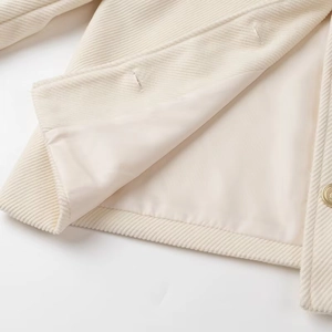 Dettaglio ravvicinato dell'orlo della giacca in lana beige con fodera e bottone dorato
