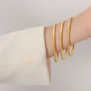 Detailed view of three minimalist gold-plated titanium steel bangles on a model's wrist