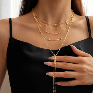 Detail of layered gold necklace featuring a zircon-studded cross pendant on a Y-shaped chain
