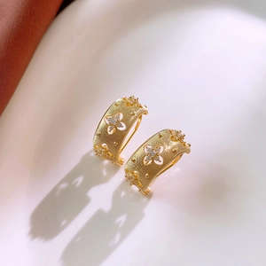 Vue macro de boucles d'oreilles fleurs dorées avec texture mate et pierres de zircon