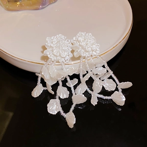 Detailed view of French-style white floral earrings with leaf charms and pearl bead tassels
