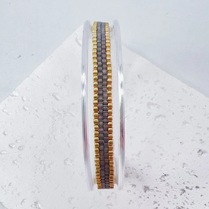 Macro detail of handmade woven Miyuki seed bead texture in gold and grey tones