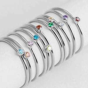 Close-up of thin silver rings with vibrant colorful inset stones on white background.