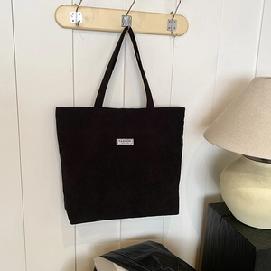 Detailed close-up of black corduroy tote bag hanging on a white wooden hook