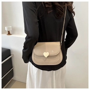 Detail of cream patent leather saddle bag with heart-shaped buckle and gold chain strap