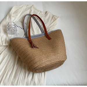 Flat lay of a woven straw tote bag with brown leather handles and fringe detail