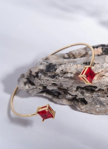 Detail of gold-plated open bangle featuring square red zircon stones on rock