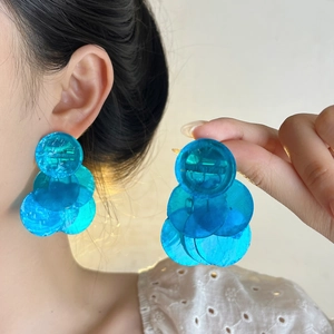 Macro view of blue layered shell-like round resin earrings worn with tassels