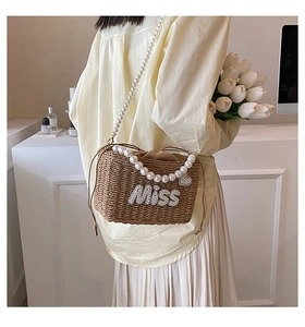 Detail of a brown woven beach bag featuring pearl handles and Miss letter decoration