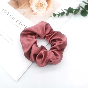 Detail of burgundy satin scrunchie with silky texture and folds on magazine prop