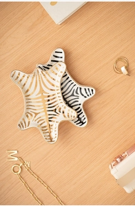 Detailed view of ceramic zebra print jewelry trays with gold edges on wood surface