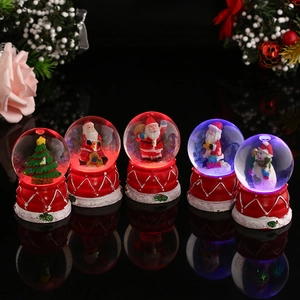 Detail of five glowing Christmas snow globes with Santa and tree inside on black surface