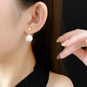 Détail d'une boucle d'oreille goutte dorée avec une perle mate blanche portée par un mannequin