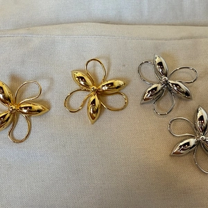 Exaggerated metal flower stud earrings in gold and silver finishes on textured fabric