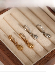 Detail of gold and silver teardrop earrings with zircon stones in a wooden jewelry box
