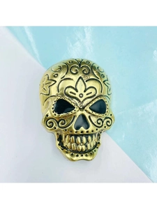 Detailed close-up of a vintage golden skull brooch with intricate black floral engravings