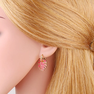 Close-up of bohemian gold hoop earrings with pink enamel monstera leaves on a model