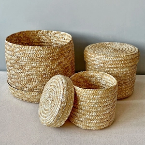Detailed view of three sizes of round woven straw storage baskets with lids in natural finish
