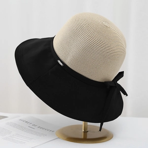 Detail of a wide black fabric brim and bow on a beige straw sun hat with metal logo