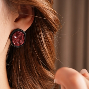 Close-up of geometric dark red resin earring with black frame worn by a model