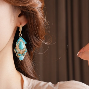 Détail de boucles d'oreilles bohèmes en turquoise avec franges dorées sur un mannequin