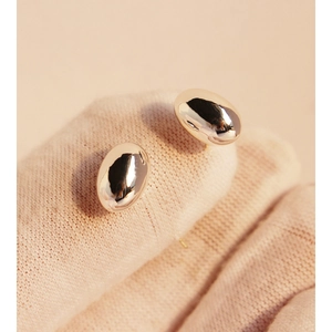 Minimalist gold oval stud earrings with high-mirror polish finish on a neutral glove background